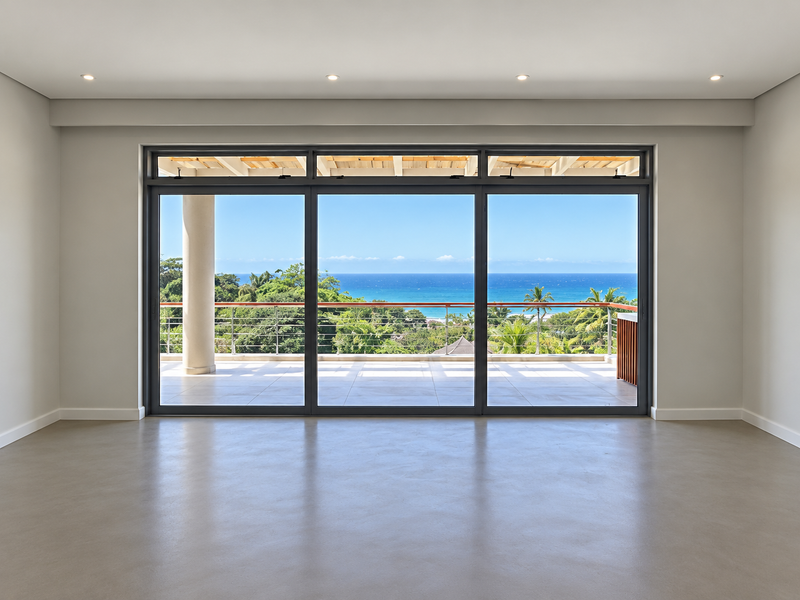 Spacious, modern living area featuring polished concrete floors, recessed lighting, and large sliding glass doors opening to a balcony with panoramic ocean views.