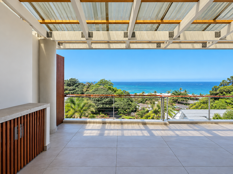 Spacious covered balcony featuring modern tiled flooring, timber pergola, built-in cabinetry, and stunning panoramic ocean views.
