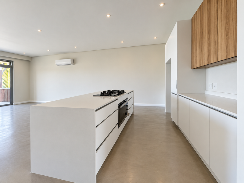 Modern open-plan kitchen featuring a central island with gas cooktop, built-in oven, sleek white cabinetry, and polished concrete floors in a spacious living area.