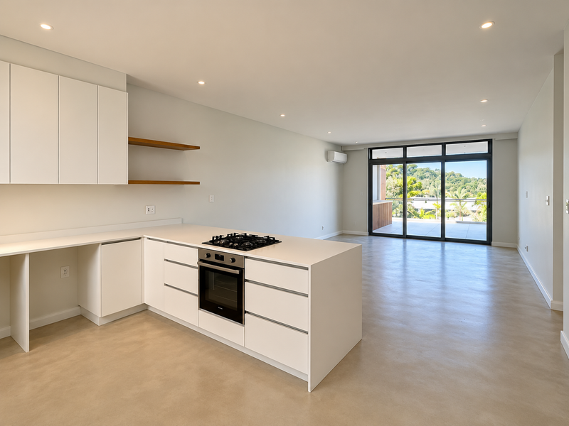 Modern open-plan kitchen and living area featuring sleek white cabinetry, integrated gas cooktop, oven, polished concrete floors, and large sliding doors leading to a balcony.