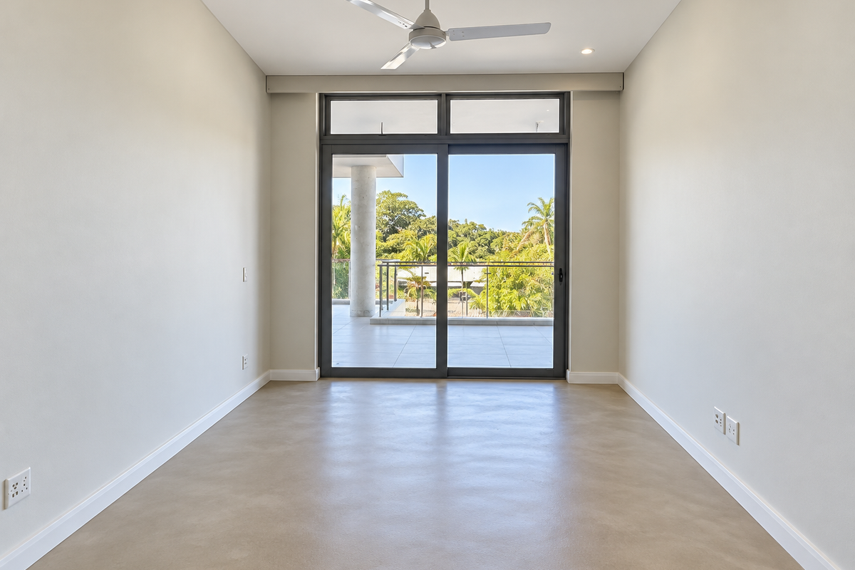 A bright, empty bedroom featuring polished concrete floors, a modern ceiling fan, and large sliding glass doors opening onto a private balcony.