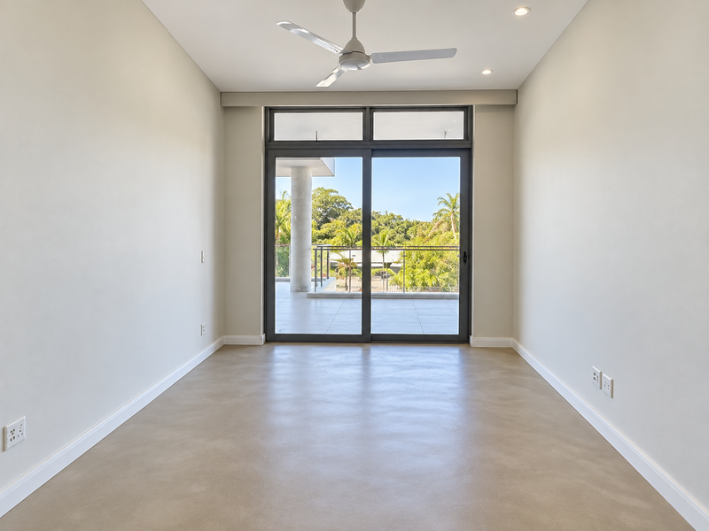 A bright, empty bedroom featuring polished concrete floors, a modern ceiling fan, and large sliding glass doors opening onto a private balcony.