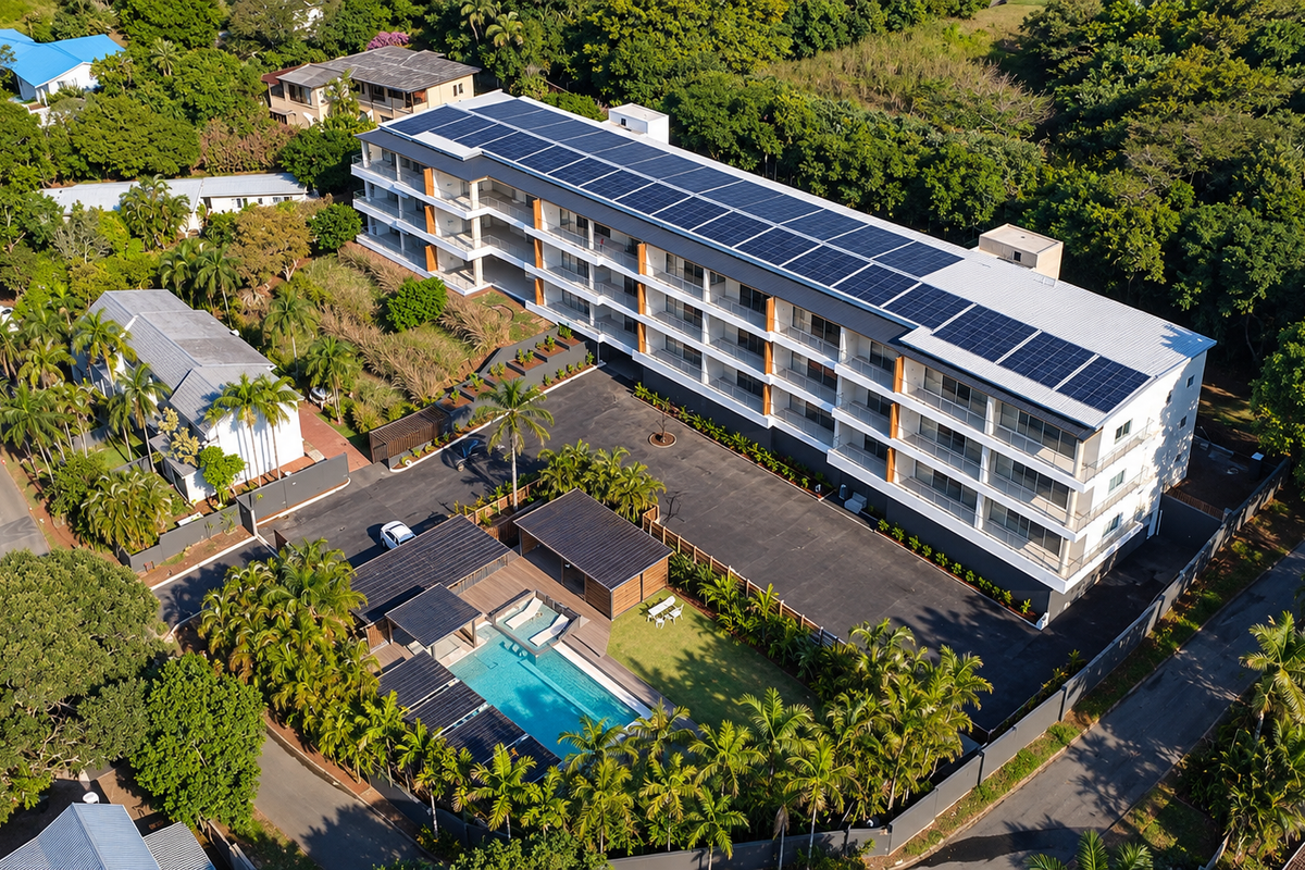Aerial view of a modern apartment complex featuring a large solar panel array, swimming pool, landscaped grounds, and ample parking facilities.