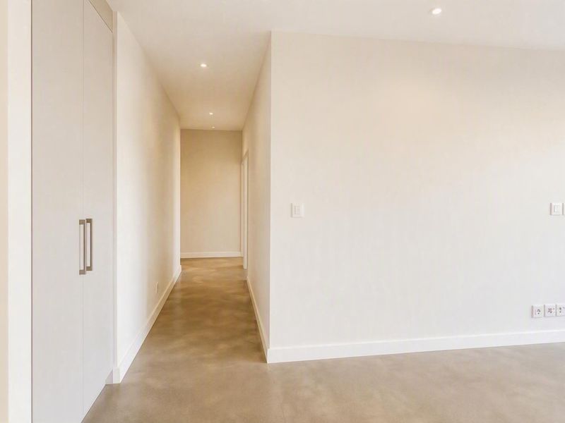 A bright, minimalist hallway featuring polished concrete flooring, recessed downlighting, and integrated built-in storage cupboards.