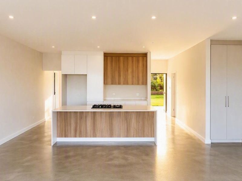 Modern open-plan living area featuring a sleek kitchen island with integrated hob, polished concrete floors, and neutral cabinetry in a bright, spacious layout.