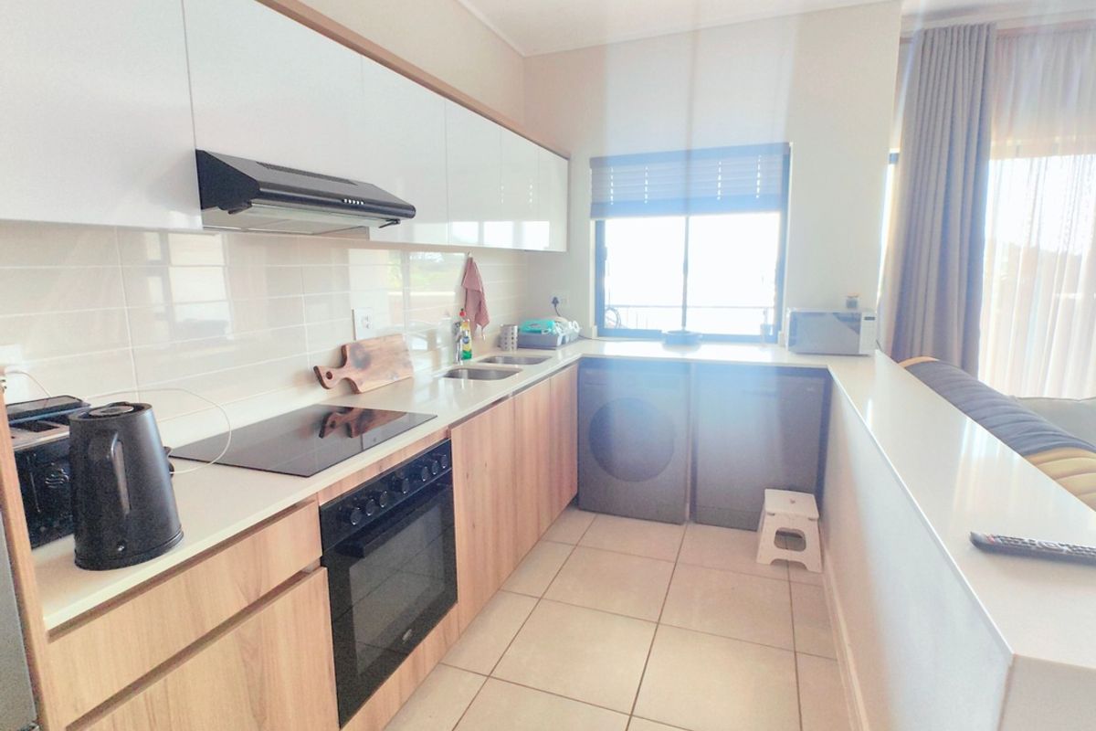 Modern kitchen featuring light wood-tone cabinetry, white stone countertops, integrated electric hob and oven, and tiled flooring with a clean, functional layout.