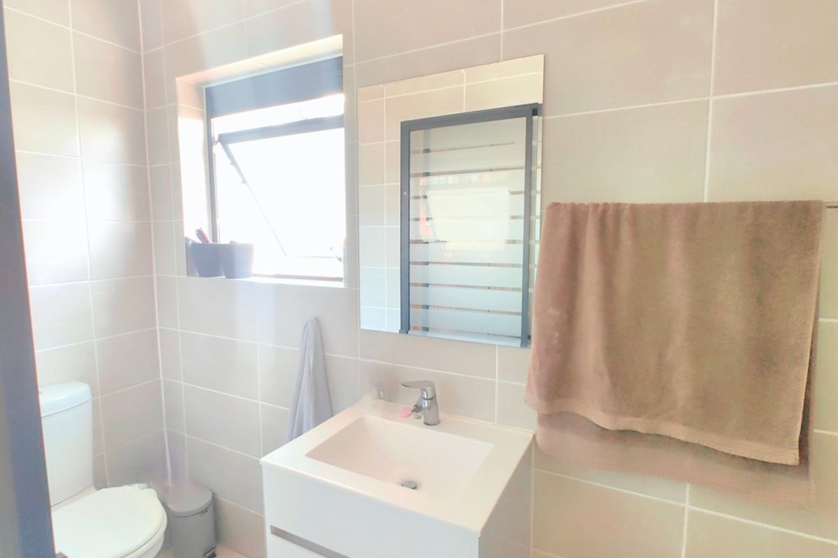 A modern, neutral-toned bathroom featuring a wall-mounted vanity with a ceramic basin, chrome fixtures, and full-height wall tiling.
