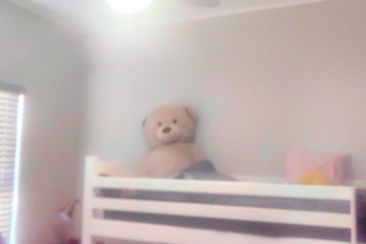 A bedroom featuring a ceiling fan and venetian blinds, captured in a low-quality, blurry photograph.