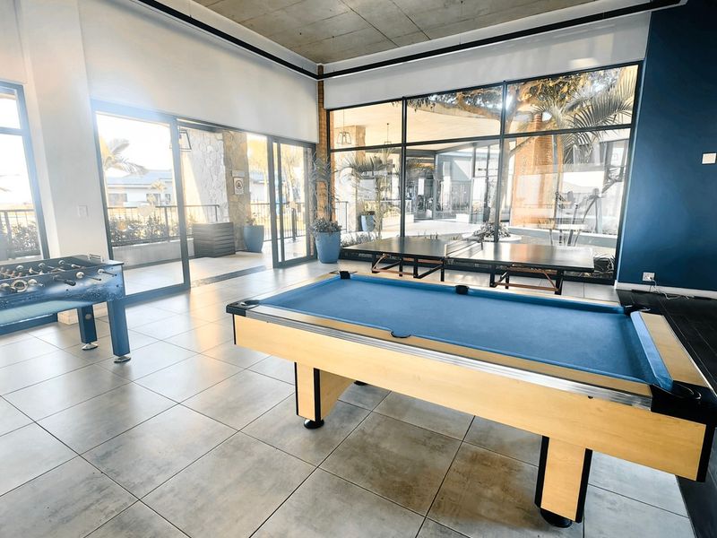 A spacious, modern clubhouse area featuring exposed concrete ceilings, large format floor tiles, and expansive glass walls providing natural light and outdoor views.