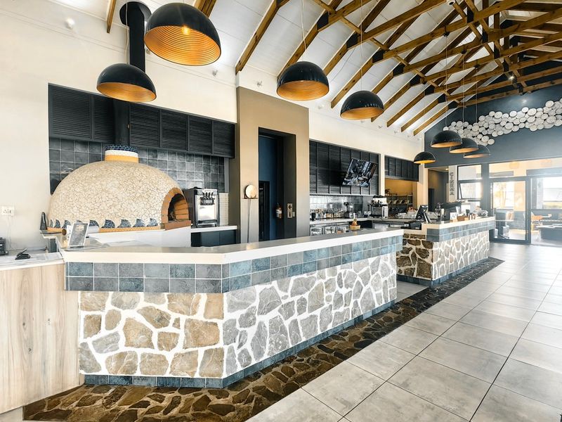 A well-maintained clubhouse interior featuring a stone-clad service counter, built-in pizza oven, and striking exposed timber roof trusses with modern pendant lighting.