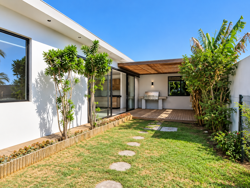 Modern rear courtyard featuring timber decking, a built-in braai area with a timber pergola, and a well-maintained landscaped garden with sliding door access.