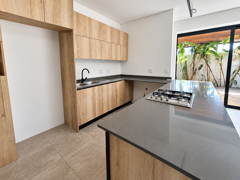 Modern kitchen featuring light wood cabinetry, stone countertops, a central island with a gas hob, and direct access to an outdoor patio area.