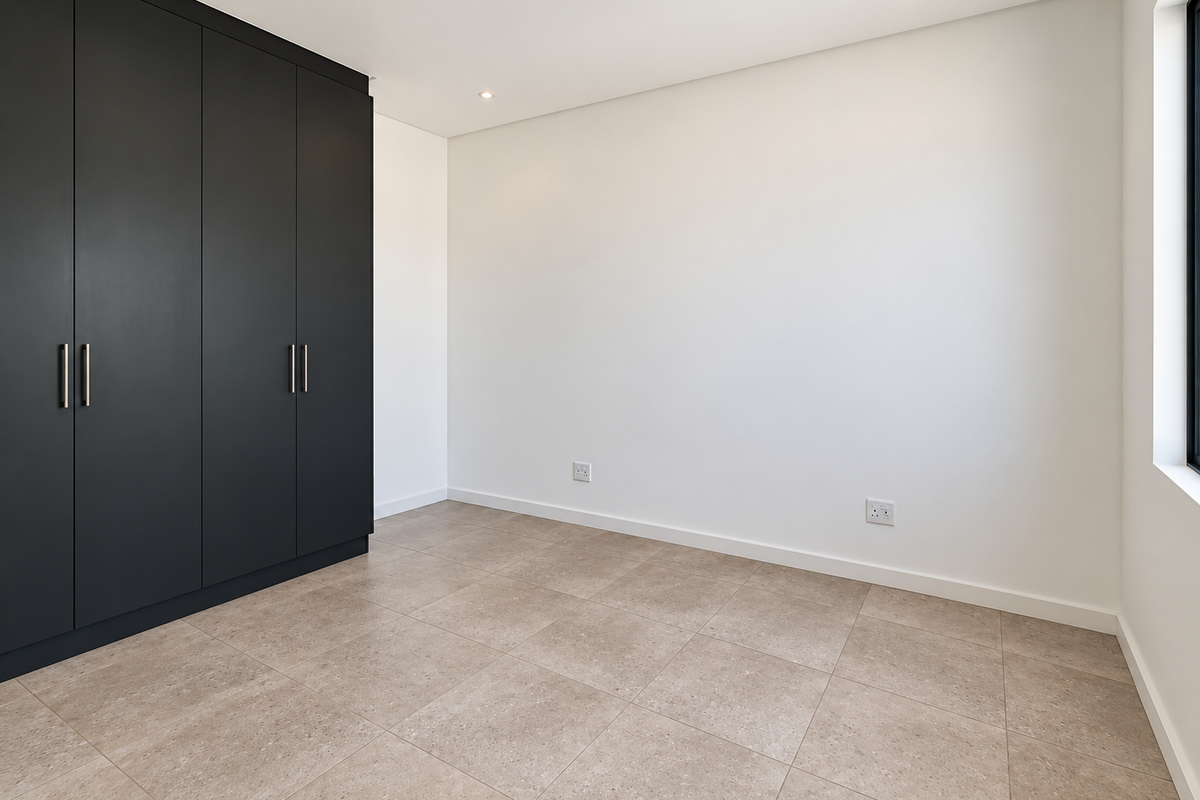 A bright, modern bedroom featuring neutral tiled flooring, clean white walls, and sleek dark built-in cupboards with recessed lighting.