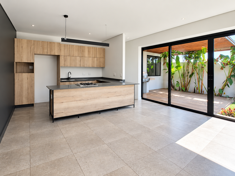 Modern open-plan kitchen featuring light wood cabinetry, a central island with a gas hob, and large sliding doors opening to a private patio area.