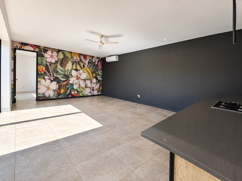Spacious open-plan living area featuring large-format floor tiles, a modern kitchen island with gas cooktop, split-system air conditioning, and a decorative floral feature wall.