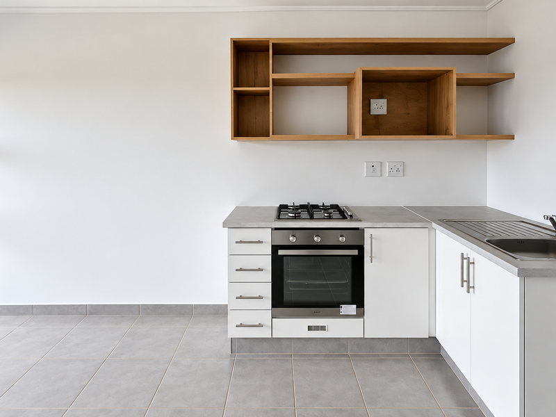 A clean, modern kitchen featuring white cabinetry, built-in oven, gas hob, stainless steel sink, and open wooden shelving against a neutral backdrop.