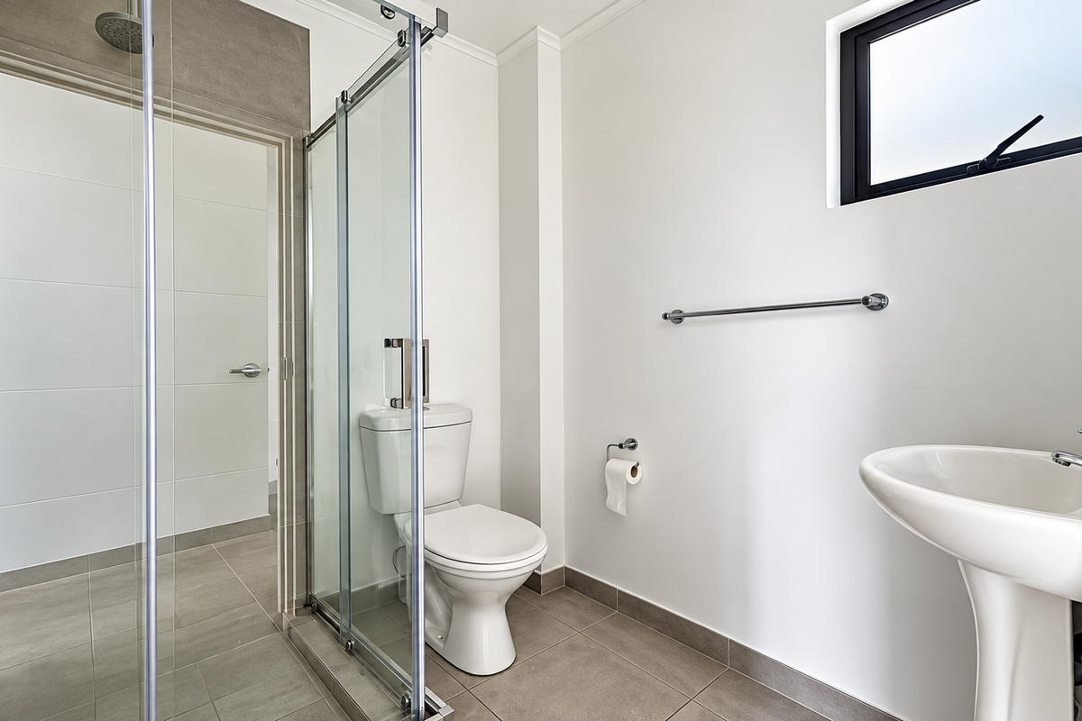A clean, modern bathroom featuring a pedestal basin, a glass-enclosed shower, and neutral floor tiling with a functional layout.