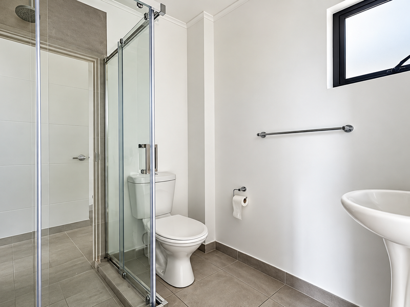A clean, modern bathroom featuring a pedestal basin, a glass-enclosed shower, and neutral floor tiling with a functional layout.