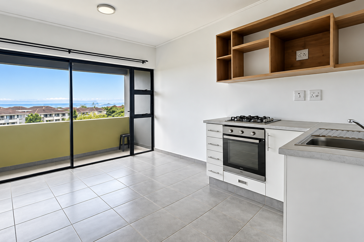 Modern open-plan kitchen area featuring built-in cabinetry, gas hob, oven, and direct access to a balcony with scenic coastal views.