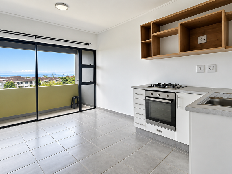 Modern open-plan kitchen area featuring built-in cabinetry, gas hob, oven, and direct access to a balcony with scenic coastal views.