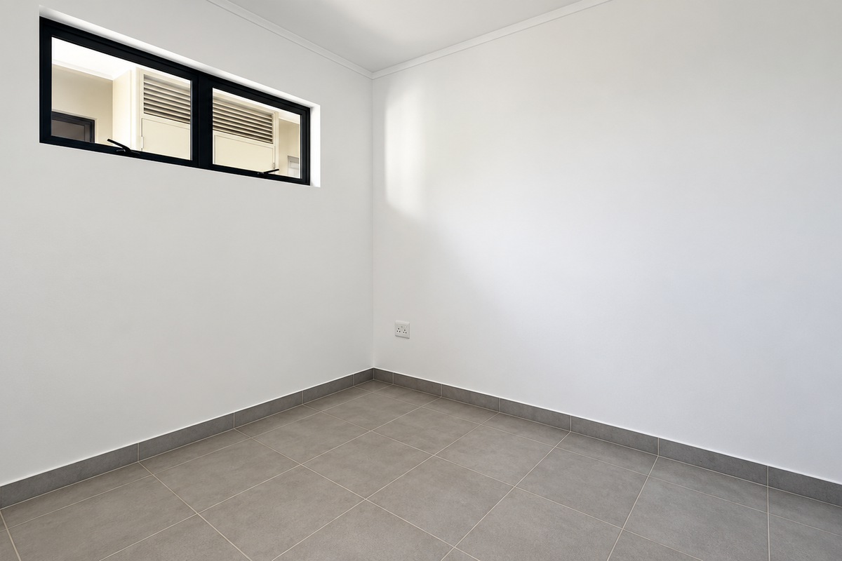 A clean, empty bedroom featuring neutral tiled flooring, crisp white walls, and a modern black aluminium window frame.