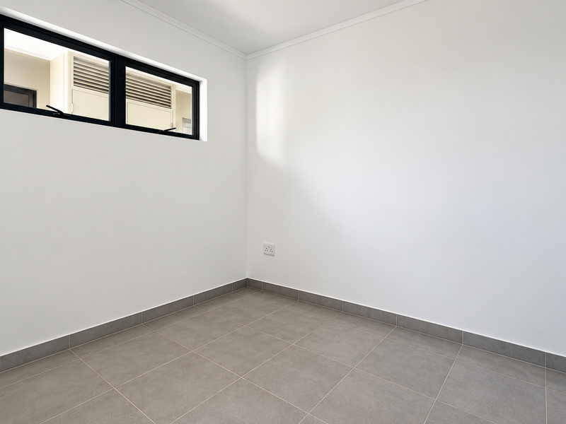 A clean, empty bedroom featuring neutral tiled flooring, crisp white walls, and a modern black aluminium window frame.