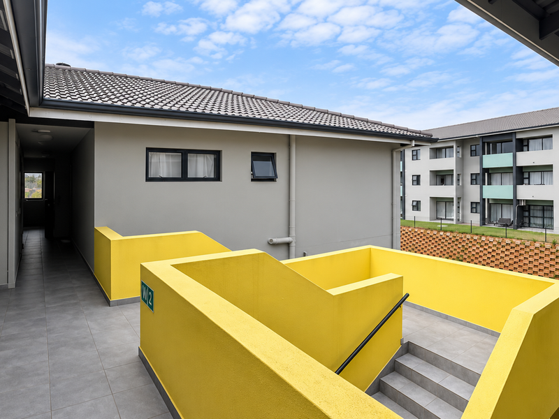 Exterior view of an apartment complex featuring a tiled staircase with a bright yellow balustrade and a covered walkway.