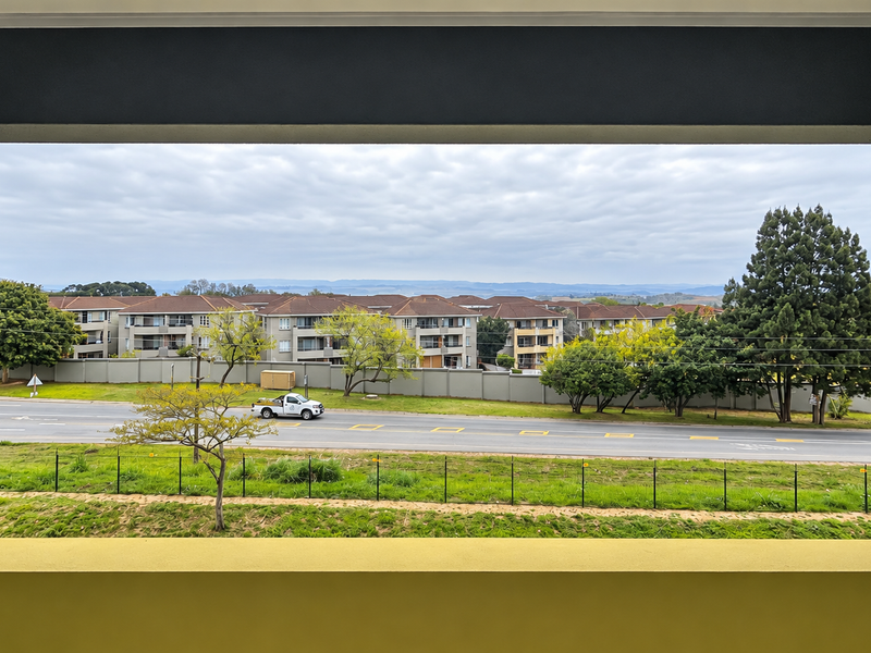 A clear elevated view overlooking a suburban road, surrounding apartment complexes, and landscaped greenery from a private balcony.