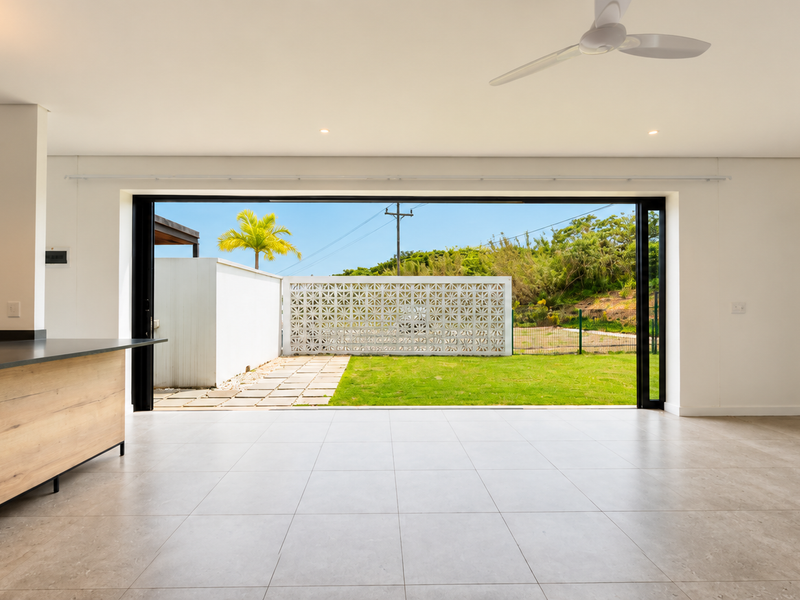 Spacious open-plan living area featuring modern tiled floors, a sleek kitchen island, and large sliding doors opening to a private garden with breeze block wall.