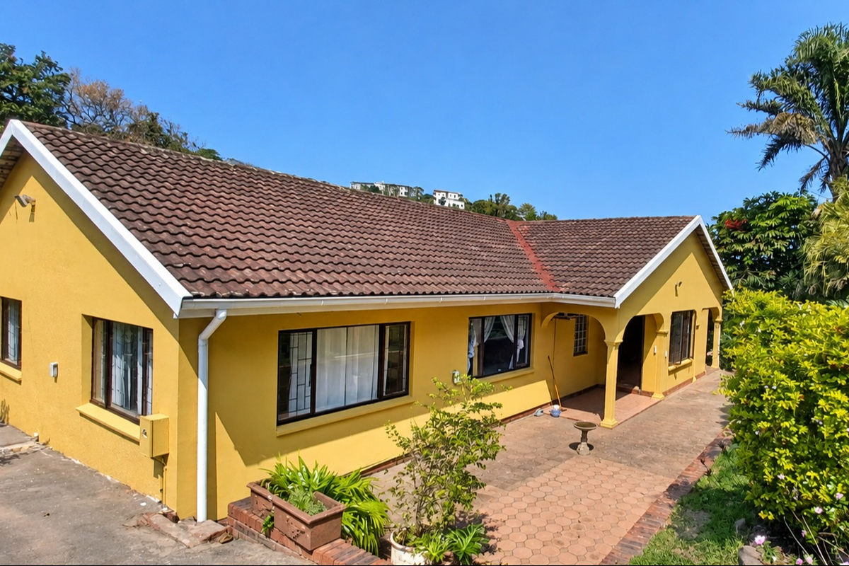 Rear view of a yellow-painted house featuring a tiled roof, paved patio area, and an arched entrance.