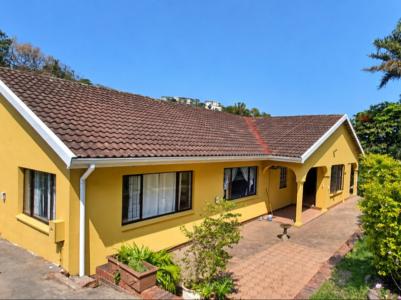 Rear view of a yellow-painted house featuring a tiled roof, paved patio area, and an arched entrance.