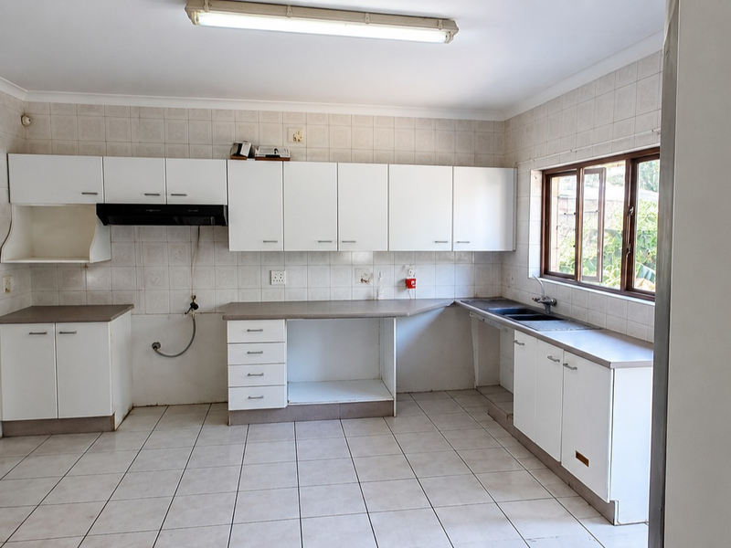 A functional, empty kitchen featuring white built-in cabinetry, laminate countertops, a double basin sink, and tiled finishes throughout.