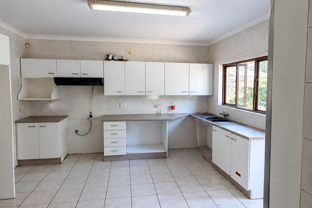 A functional, empty kitchen featuring white built-in cabinetry, laminate countertops, a double basin sink, and tiled finishes throughout.