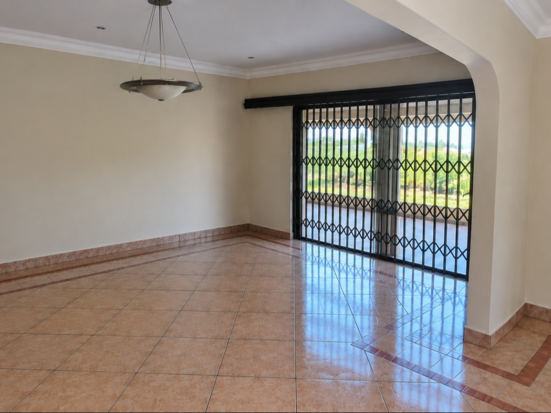 Spacious, empty living area featuring ceramic tile flooring, decorative border detailing, and a sliding glass door with a security gate leading to the outdoors.