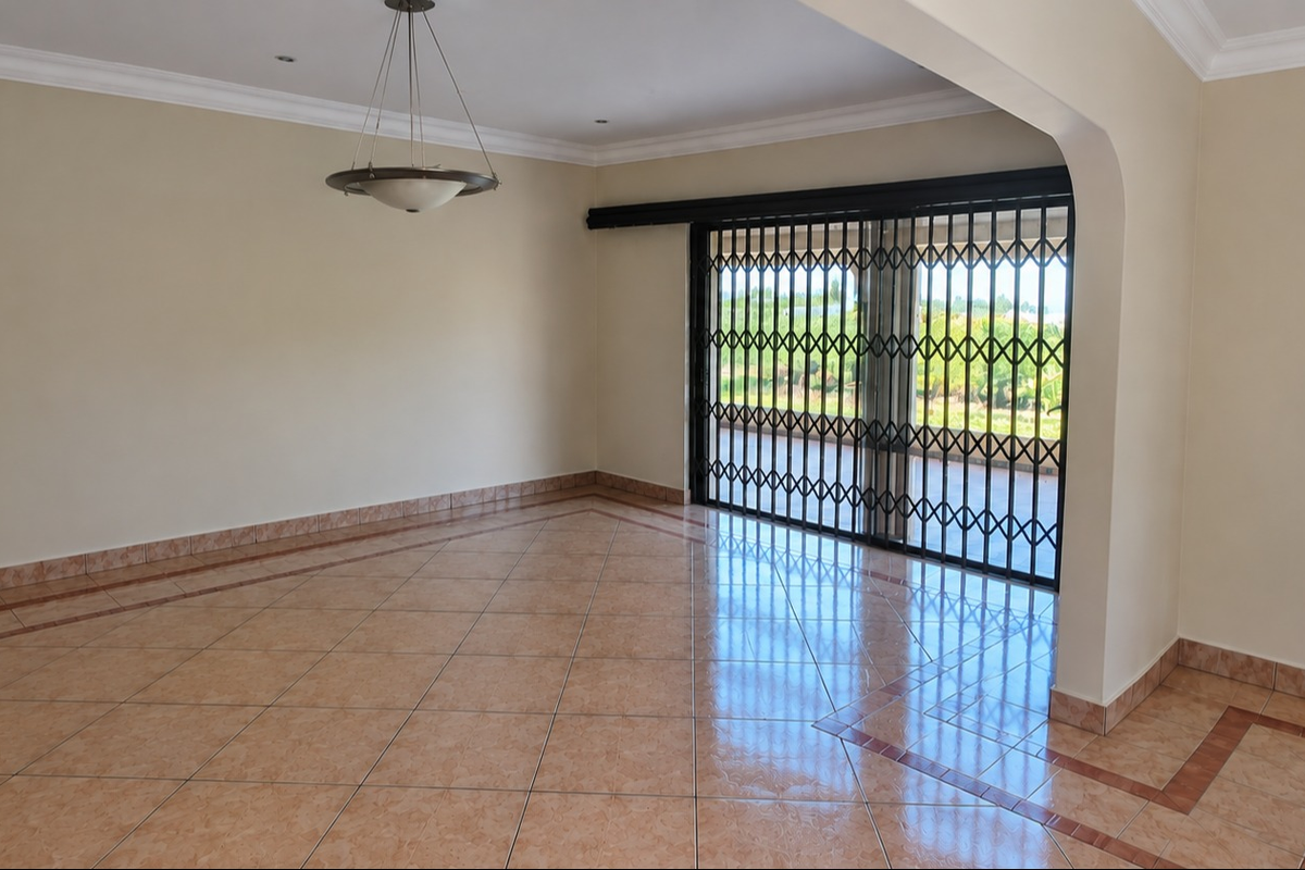 Spacious, empty living area featuring ceramic tile flooring, decorative border detailing, and a sliding glass door with a security gate leading to the outdoors.