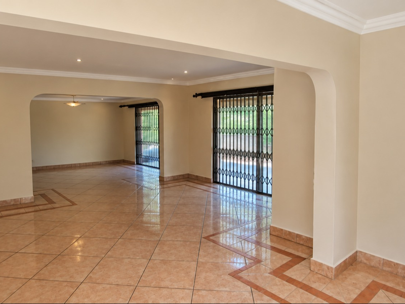Spacious open-plan living area featuring neutral walls, ceramic tile flooring with decorative borders, and a unique glass block feature window.