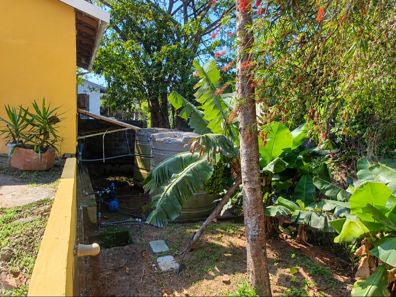Rear exterior area featuring a water storage tank, pump system, and concrete paving adjacent to the yellow building facade.