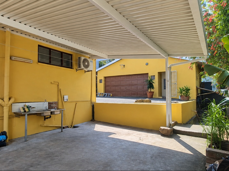 A covered outdoor patio area featuring a built-in stainless steel sink, concrete flooring, and direct access to the rear yard and garage.