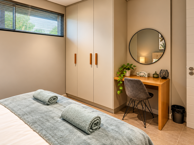 A modern, well-maintained bedroom featuring built-in cupboards, tiled flooring, and a high-level horizontal window with integrated blinds.
