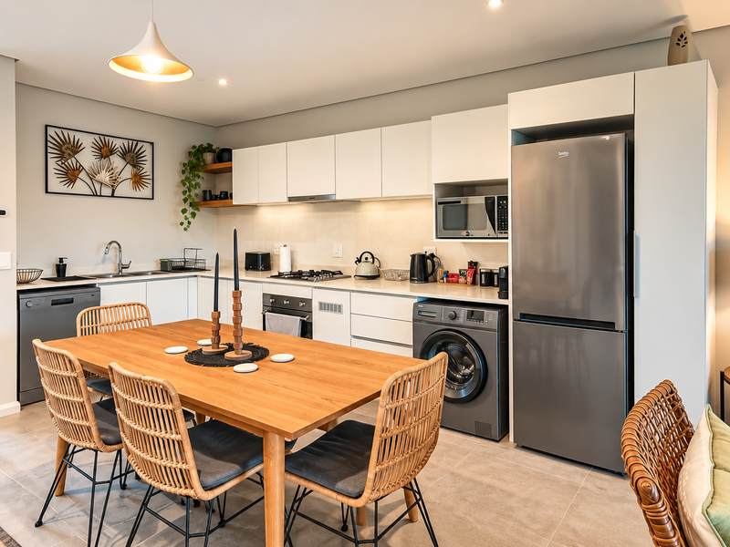 Modern open-plan kitchen and dining area featuring sleek cabinetry, integrated appliances, tiled flooring, and direct access to a balcony.