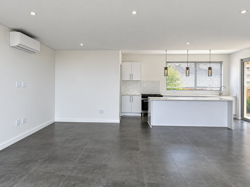 Spacious open-plan living and kitchen area featuring modern tiled floors, sleek white cabinetry, a central island, and direct access to an outdoor patio.