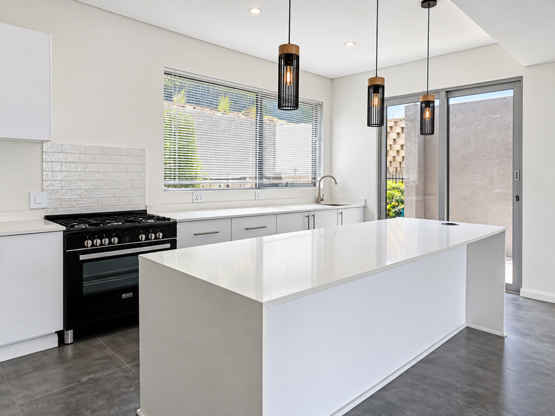 Modern kitchen featuring a central island, quartz countertops, gas stove, subway tile backsplash, and direct access to an outdoor patio area.