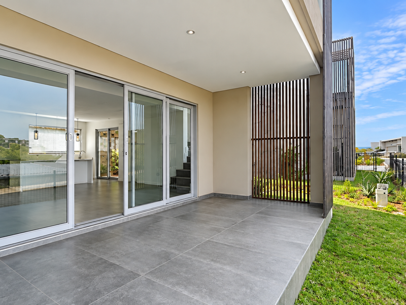 A modern covered patio featuring large sliding glass doors, sleek tiled flooring, and a decorative timber privacy screen overlooking a landscaped garden area.