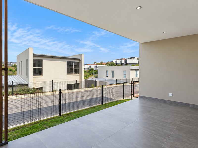 A modern, covered patio featuring large-format grey floor tiles, recessed lighting, and a timber privacy screen, overlooking the surrounding townhouse complex.