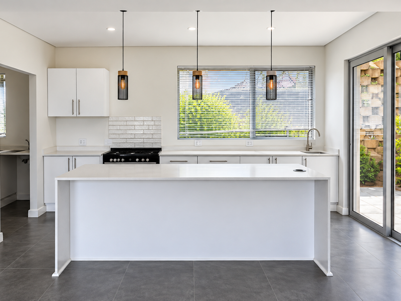 Modern, bright kitchen featuring a central island, built-in appliances, subway tile backsplash, and large sliding doors opening to a private rear patio area.