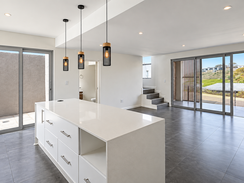 Spacious open-plan living and kitchen area featuring a modern island, sleek tiled floors, and large sliding doors leading to outdoor spaces.