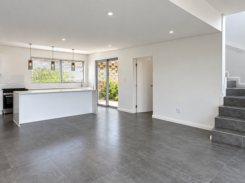 Spacious open-plan kitchen and living area featuring modern cabinetry, a central island, tiled flooring, and a staircase leading to the upper level.