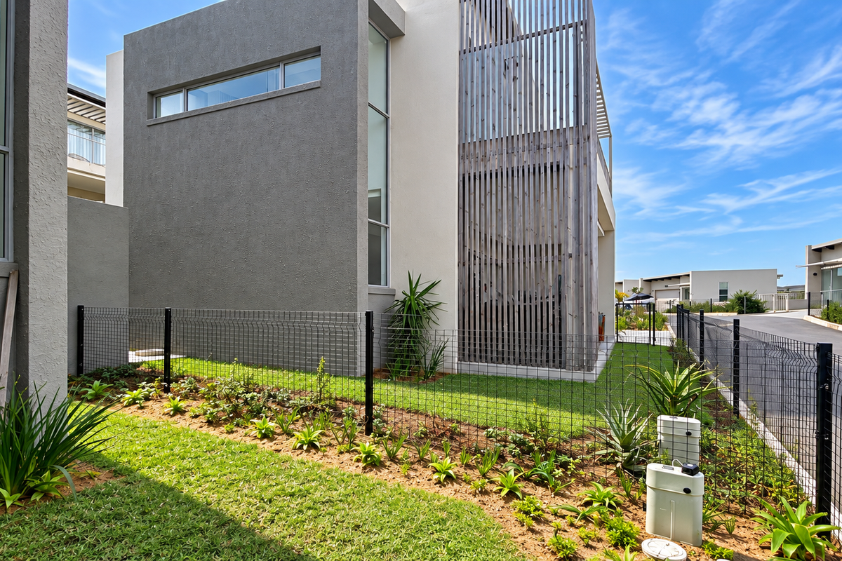 A modern townhouse exterior featuring a landscaped garden, wire mesh fencing, and a timber slat privacy screen alongside a paved driveway.