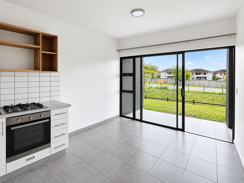 Modern open-plan kitchen area featuring built-in oven, gas hob, tiled flooring, and large sliding doors opening onto a private patio and garden.