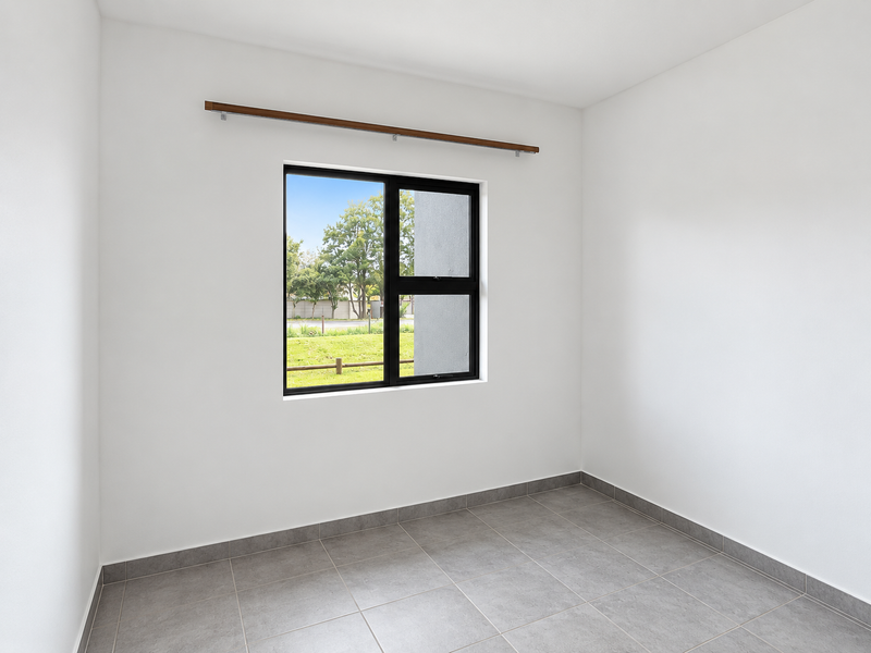 A bright, empty bedroom featuring neutral tiled flooring, white walls, and a black aluminium window frame with an integrated curtain rod.